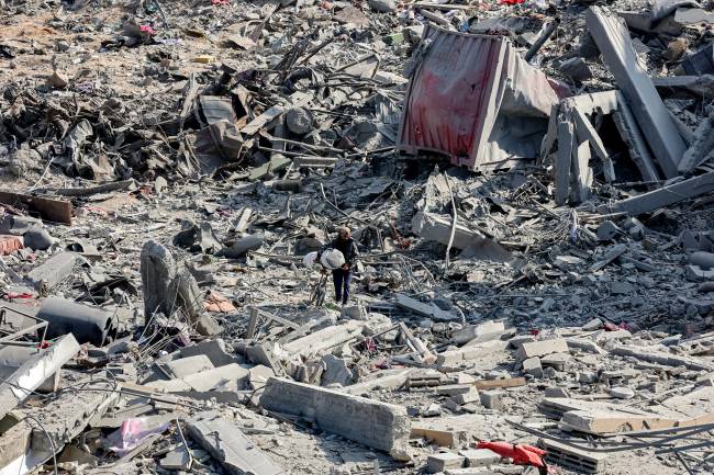 PALESTINIAN-ISRAEL-CONFLICT A man balances salvaged items atop a bicycle as he maneuvers his way through the debris and rubble of a collapsed building in Beit Lahia in the northern Gaza Strip on January 20, 2025 a day after a ceasefire deal in the war between Israel and Hamas went into effect. (Photo by Omar AL-QATTAA / AFP)