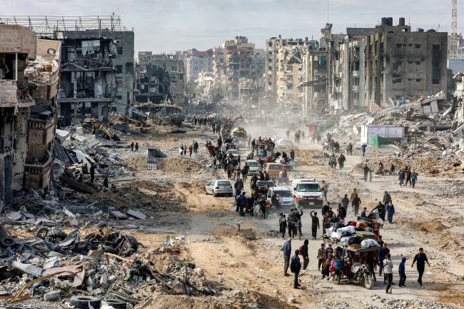PALESTINIAN-ISRAEL-CONFLICT People walk past the rubble of collapsed buildings along Saftawi street in Jabalia in the northern Gaza Strip on January 20, 2025 a day after a ceasefire deal in the war between Israel and Hamas went into effect. (Photo by Omar AL-QATTAA / AFP)