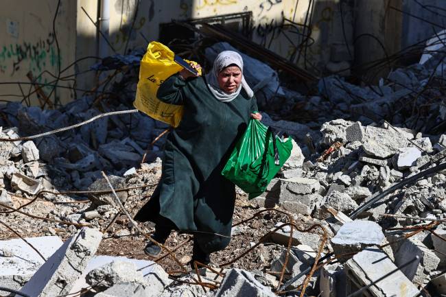 PALESTINIAN-ISRAEL-WAR A woman carries bags as she walks on rubble at the Nur Shams camp for Palestinian refugees near Tulkarem, where Israeli forces allowed residents to retrieve belongings after issuing reported demolition notifications for several houses, amid a weeks-long offensive in the occupied West Bank on February 26, 2025. (Photo by Zain JAAFAR / AFP)