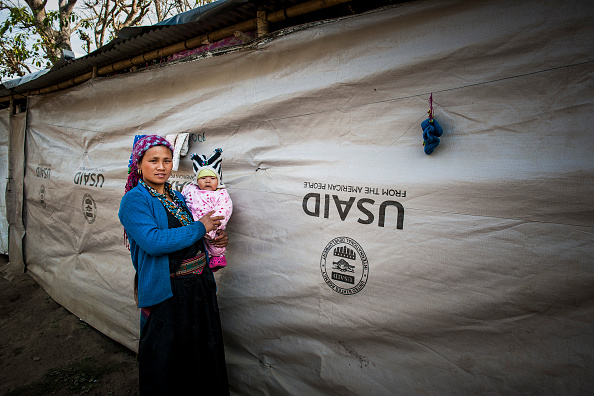 Mulher segura criança em frente a uma tenda da USaid no Nepal.