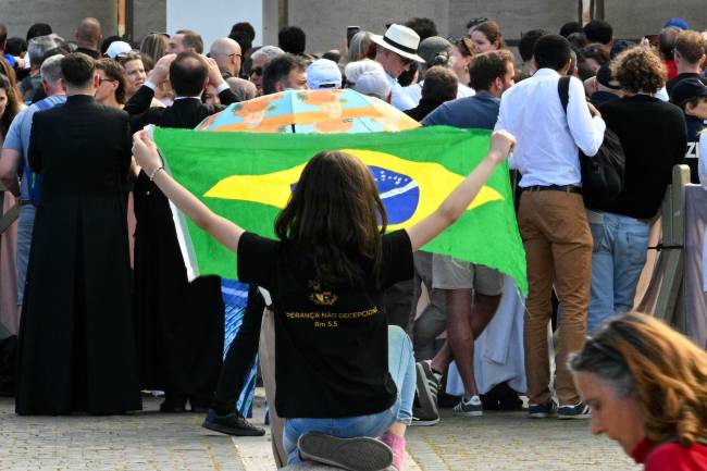 VATICAN-RELIGION-POPE-CONCLAVE A woman waves a Brazilian flag as faithful wait at St Peter's Square for smoke to rise from the chimney of the Sistine Chapel signalling the result of a conclave vote, in The Vatican, on May 7, 2025. (Photo by Andreas SOLARO / AFP)