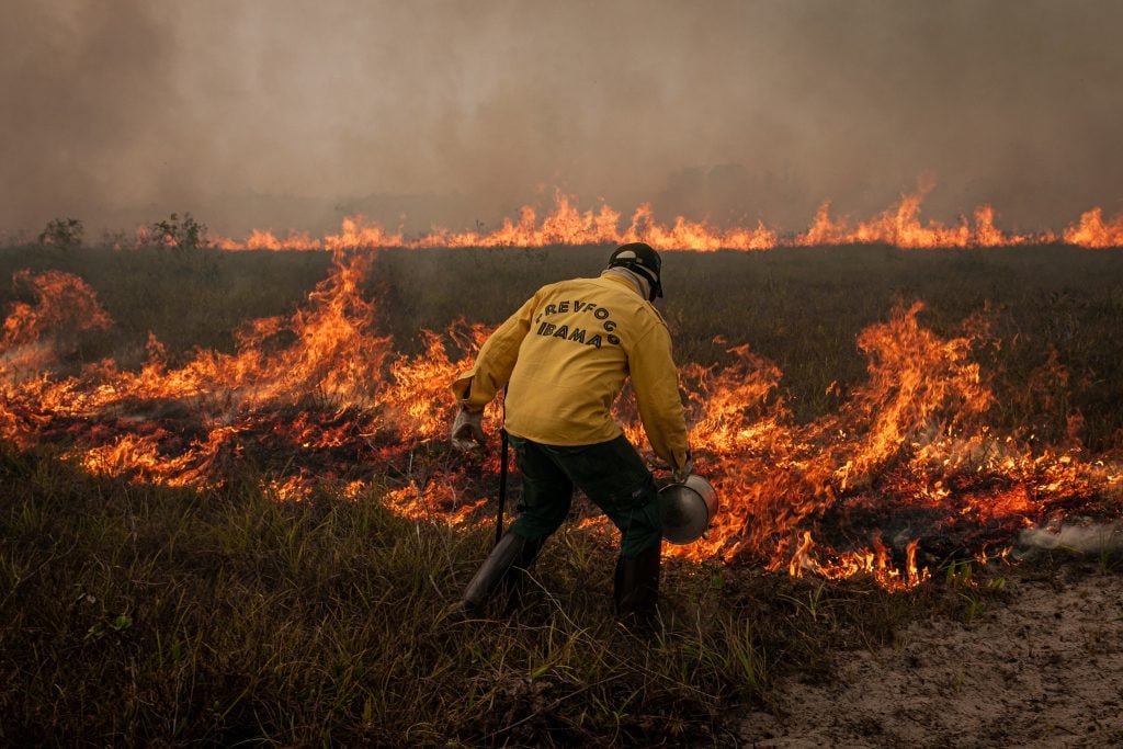 Agente do Ibama com uniforme amarelo extinguindo incêndio