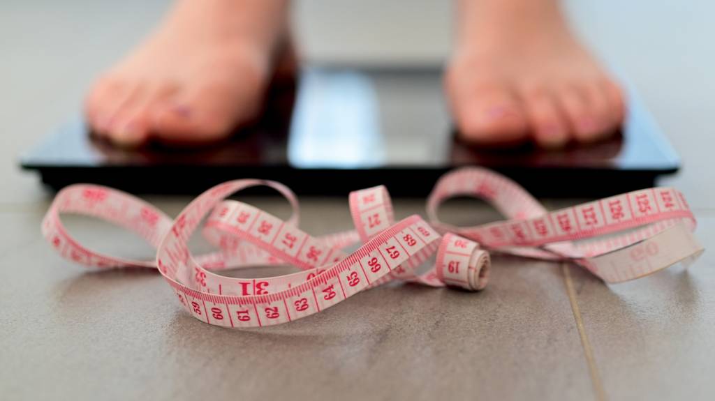 Woman measuring herself on a scale put weight PRÓXIMAS CENAS - Novas drogas para emagrecer: a revolução continua