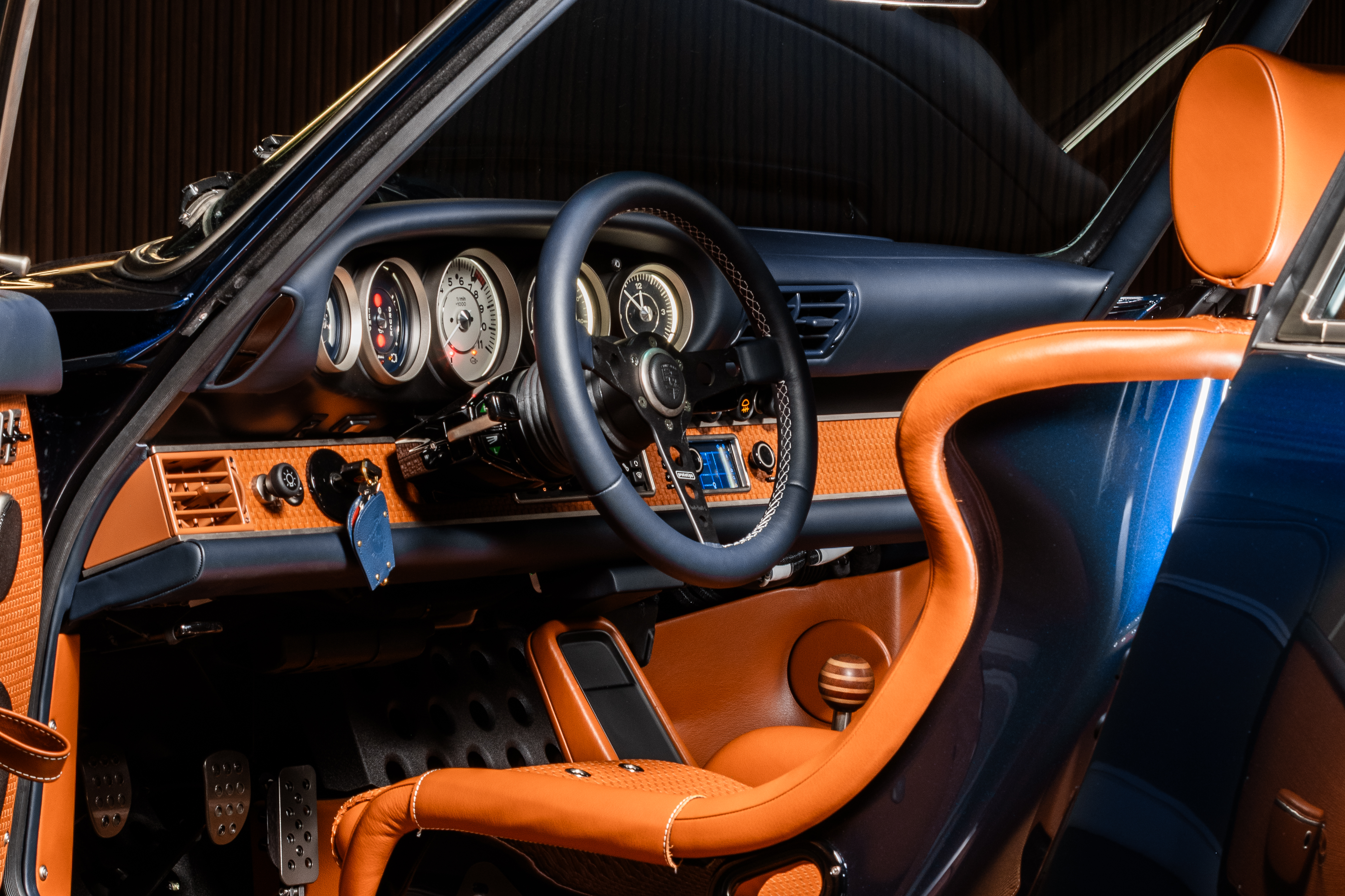 Interior do carro, com volante de três raios e bancos em couro caramelho