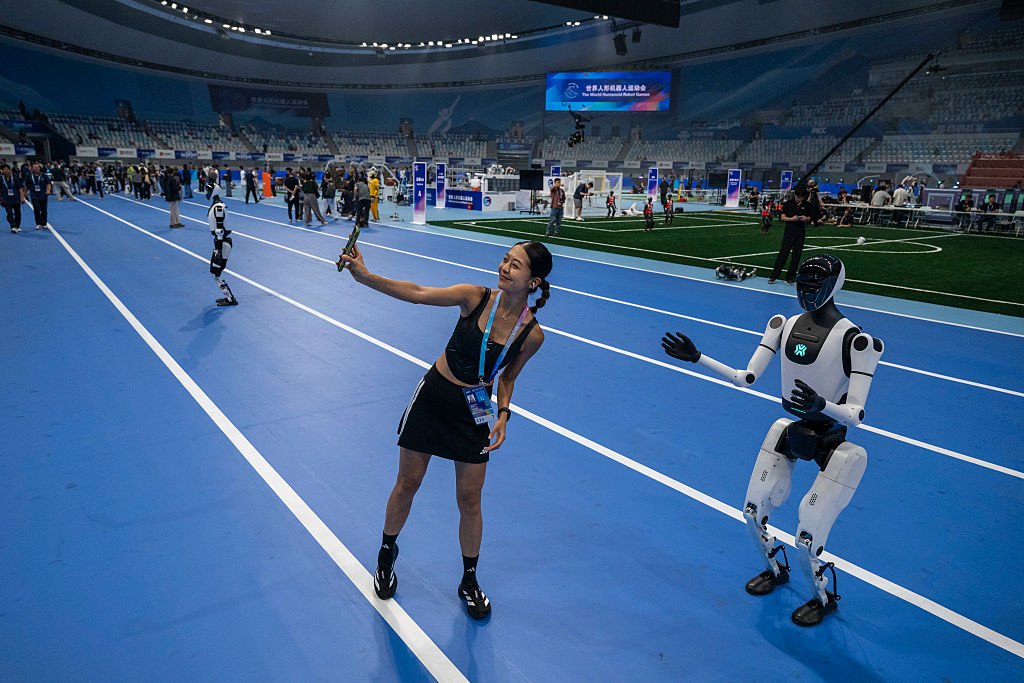 BEIJING, CHINA - AUGUST 14: A woman poses with a humanoid robot on the track at the opening ceremony of the World Humanoid Robot Games at the National Speed Skating Oval on August 14, 2025 in Beijing, China. China is holding the event from August 14-17, billed as the first of its kind. (Photo by Kevin Frayer/Getty Images)