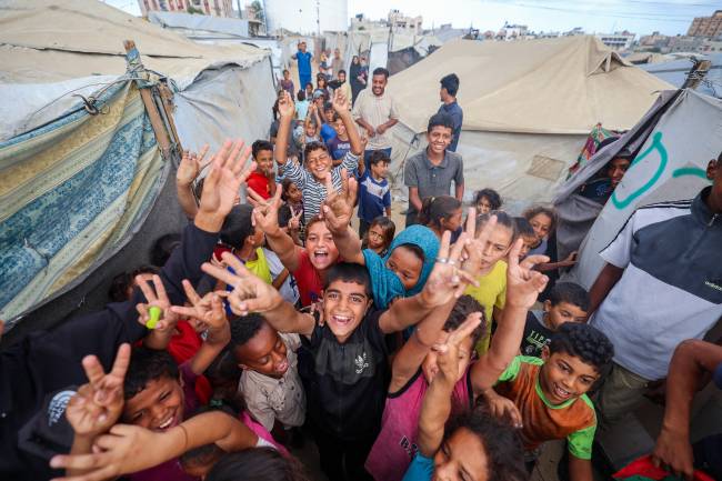 PALESTINIAN-ISRAEL-GAZA-CONFLICT Palestinian children celebrate at a camp for displaced people in Nuseirat in the central Gaza Strip on October 9, 2025, following news of a new Gaza ceasefire deal. Israel and Hamas on October 9 agreed a Gaza ceasefire deal to free the remaining living hostages, in a major step towards ending a war that has killed tens of thousands of people and unleashed a humanitarian catastrophe. (Photo by Eyad BABA / AFP)