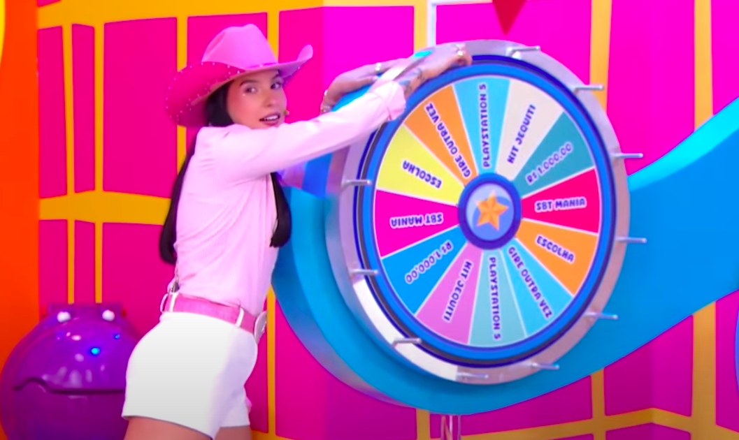 Foto da cantora Ana Castela girando uma roleta de prêmios no programa infantil Bom Dia & Cia