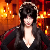 Foto da atriz Cassandra Peterson caracterizada como Elvira, com trajes pretos e maquiagem marcada
