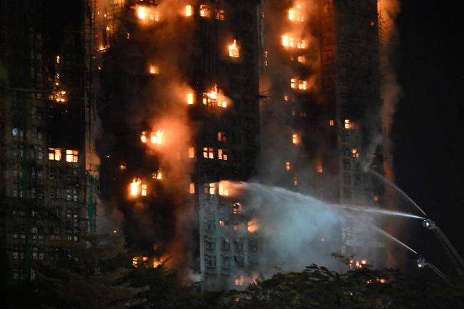 Firefighters spray water during a major fire at the Wang Fuk Court residential estate in Hong Kong's Tai Po district on November 26, 2025. At least four people were killed when a fire engulfed several high-rise blocks in a Hong Kong residential estate on November 26, the government said, with media reporting that some residents were trapped inside. (Photo by Peter PARKS / AFP)