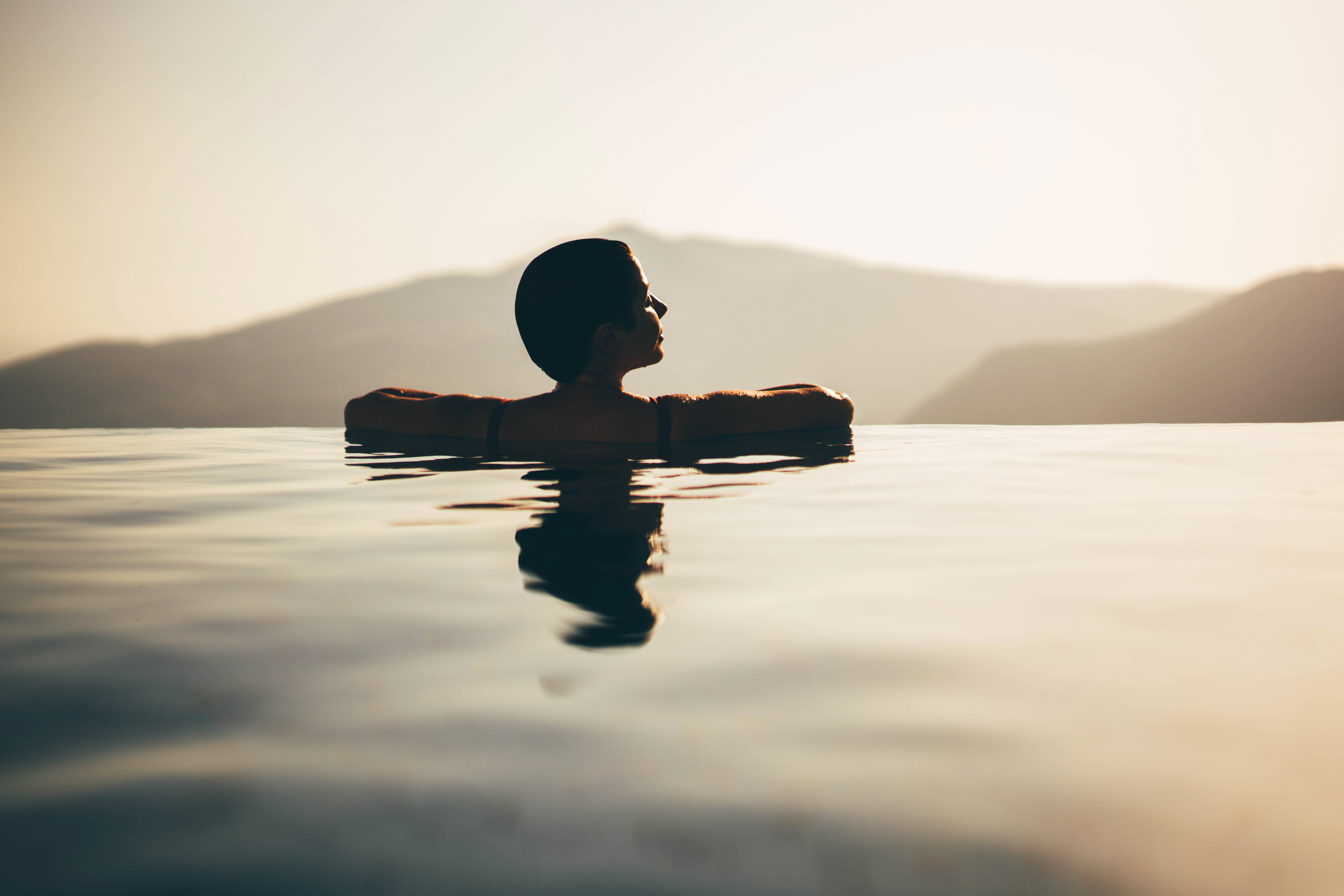 Young woman enjoying the magical view in the infinity pool at sunset.