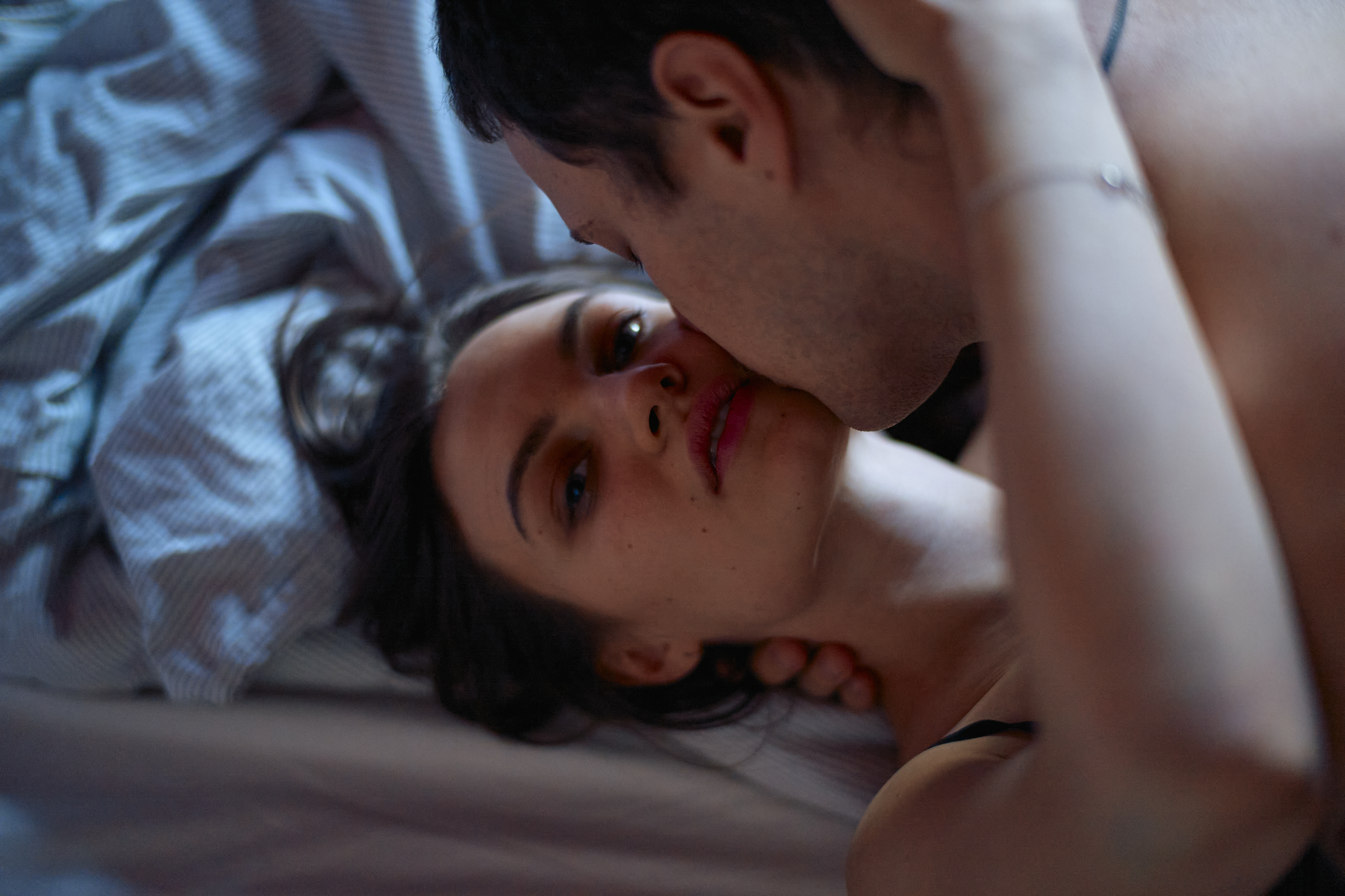 Intimate couple sharing a tender moment in bed, with a man leaning in to kiss a woman