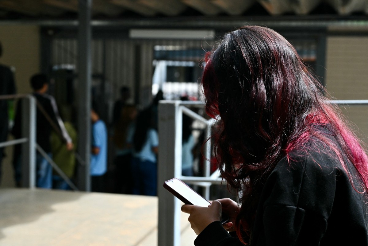 A young student uses her mobile phone at a public school in Planaltina, Brasilia on March 16, 2026. On March 17, 2026, Brazil implemented new measures restricting minors access to social media and expanding protections to prevent them from viewing violent or illegal content. The law, which went into effect, was passed last year following a scandal involving the alleged sexual exploitation of minors on Instagram in this hyperconnected country of 212 million people. (Photo by Evaristo Sa / AFP)