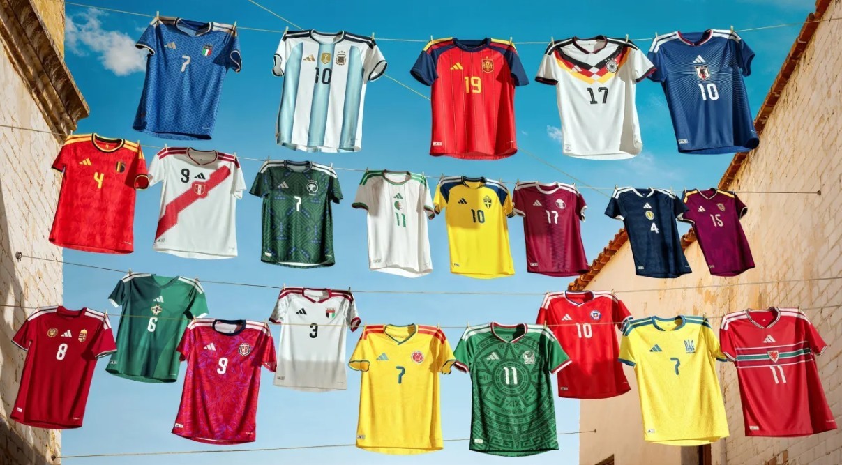 Camisas de futebol de diversas seleções, incluindo Argentina, Espanha, Japão e México, penduradas em varais sob um céu azul
