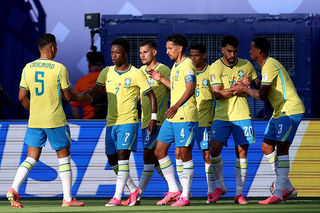 Jogadores da seleção brasileira de futebol, com camisas amarelas e shorts azuis, cumprimentam-se no campo antes de uma partida