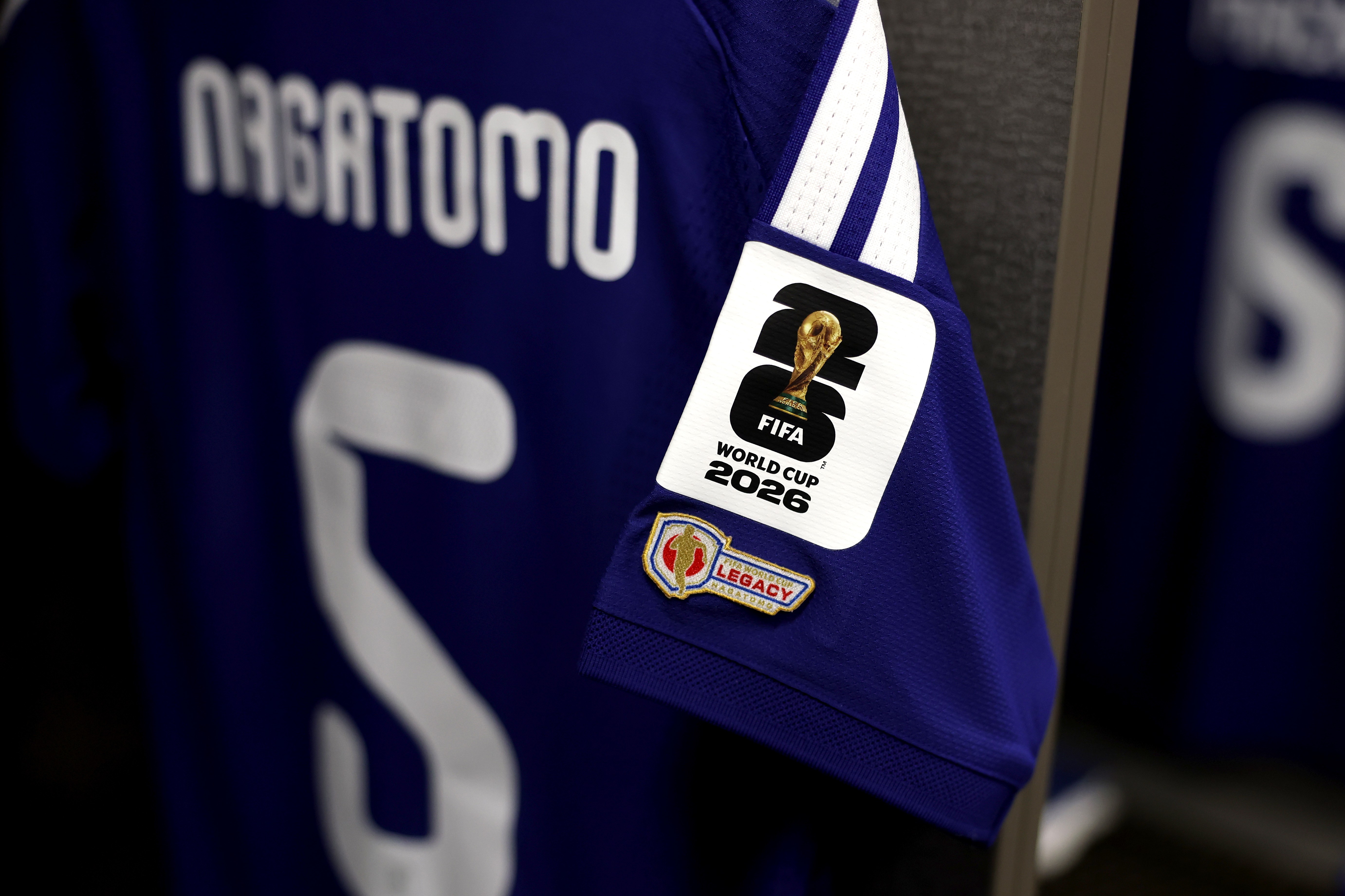Camisa de futebol azul-escura com o nome NAGATOMO e o número 5 em branco. Na manga, há um patch branco com o logo da FIFA World Cup 2026 e um patch dourado e vermelho Legacy abaixo