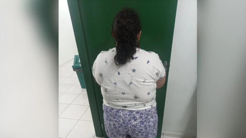 Mulher de costas, com cabelo escuro preso, vestindo camiseta branca estampada com estrelas e shorts florido, em frente a uma porta verde