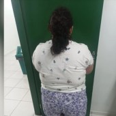 Mulher de costas, com cabelo escuro preso, vestindo camiseta branca estampada com estrelas e shorts florido, em frente a uma porta verde