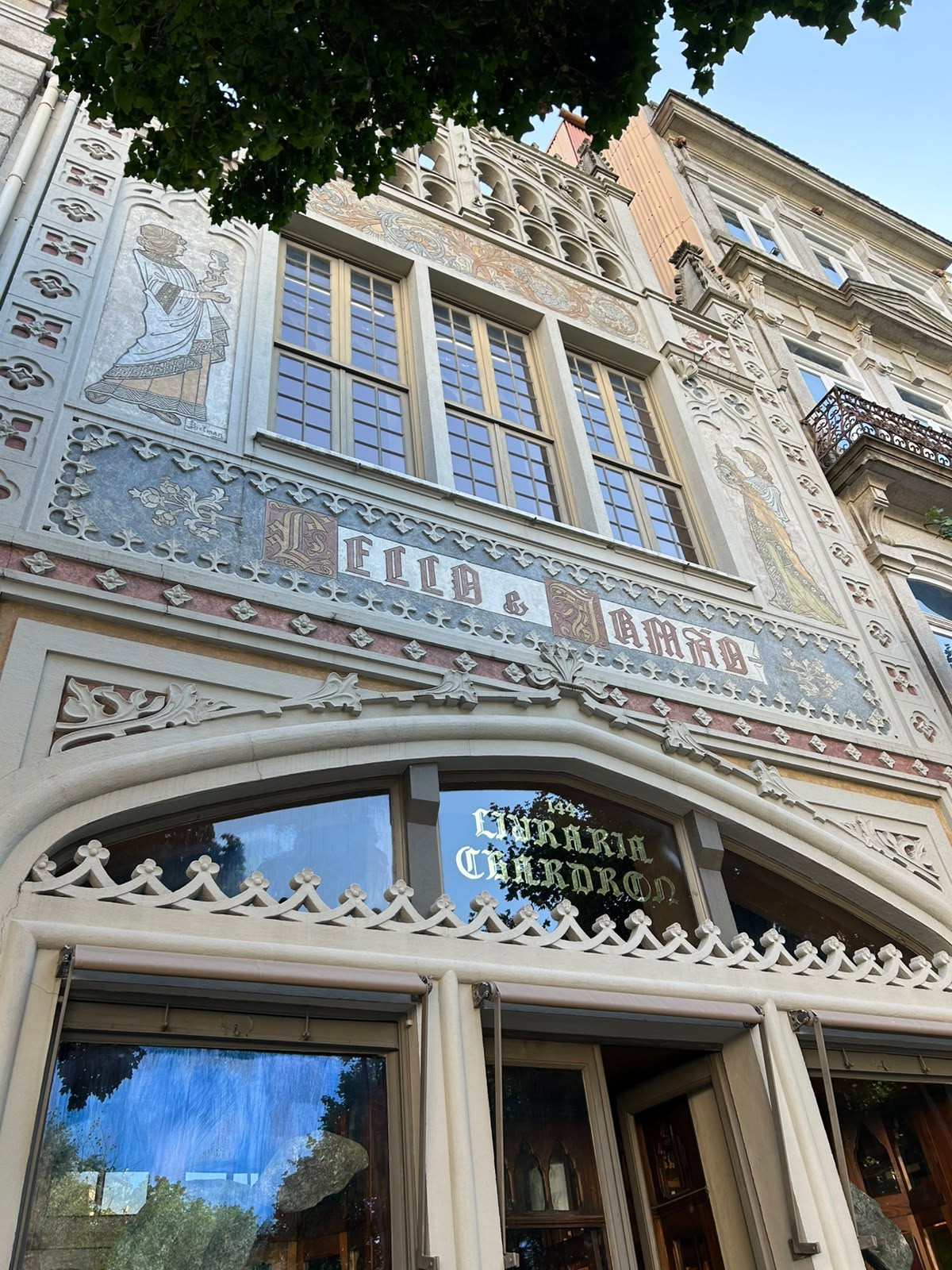 Fachada ornamentada da Livraria Lello e Irmão, com janelas altas, detalhes em relevo e painéis decorados com figuras e o nome Livraria Chardron na vitrine principal