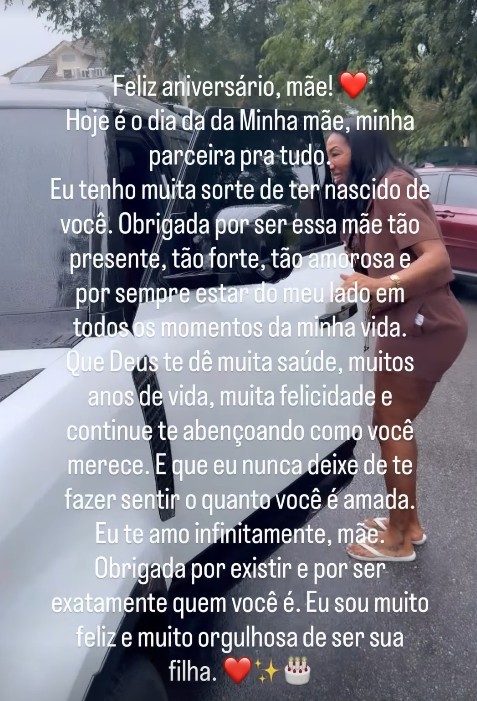Mulher de pele morena e cabelo escuro, vestindo um vestido marrom, sorri enquanto se inclina para um carro branco. Um texto de feliz aniversário para a mãe cobre a imagem.