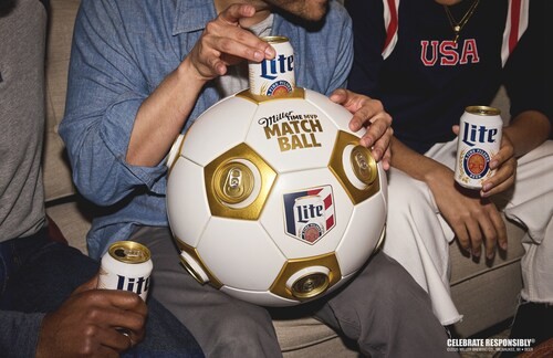 Três pessoas sentadas em um sofá, com um homem de camisa jeans segurando uma bola de futebol branca e dourada com latas de Miller Lite. Outras duas latas abertas estão nas mãos de outras pessoas, uma delas vestindo uma camisa preta com USA em vermelho