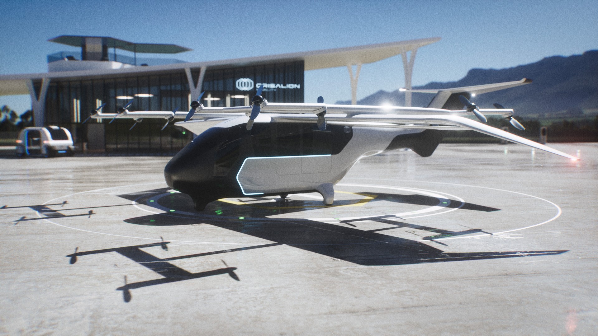 Aeronave eVTOL preta e branca com hélices em cima das asas, estacionada em uma plataforma de pouso circular. Ao fundo, um prédio moderno com o nome EVE EMBAER e montanhas sob céu azul