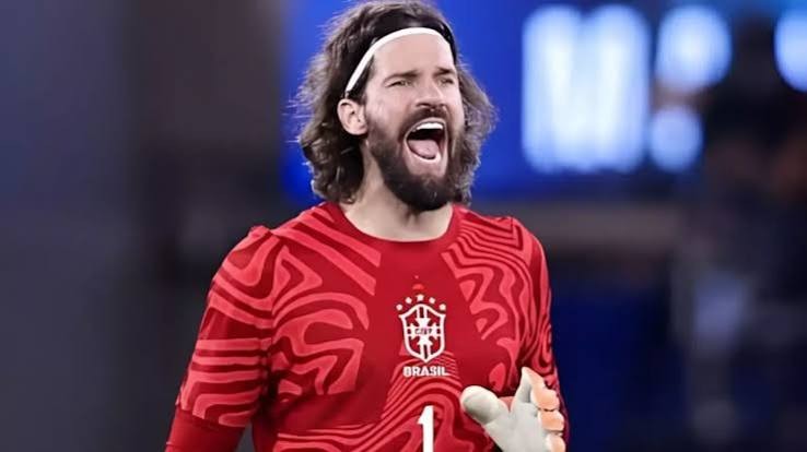 Goleiro Alisson Becker, com barba e cabelo comprido, usa uma faixa branca na cabeça e camisa vermelha da seleção brasileira com estampa abstrata, gritando com a boca aberta e expressão intensa em campo