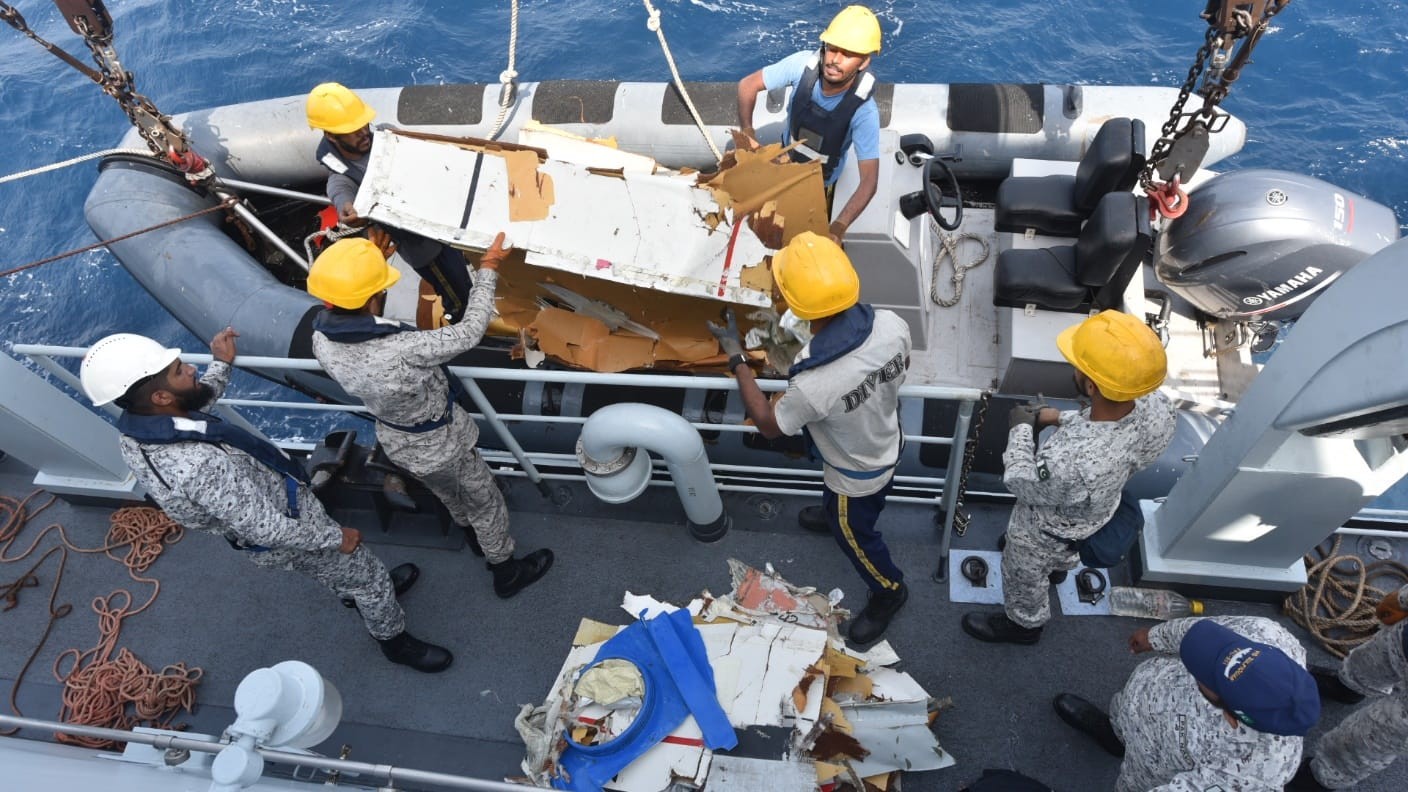 Equipe de resgate em um navio, usando capacetes de seguran&ccedil;a e coletes salva-vidas, recupera destro&ccedil;os de um barco infl&aacute;vel no mar azul