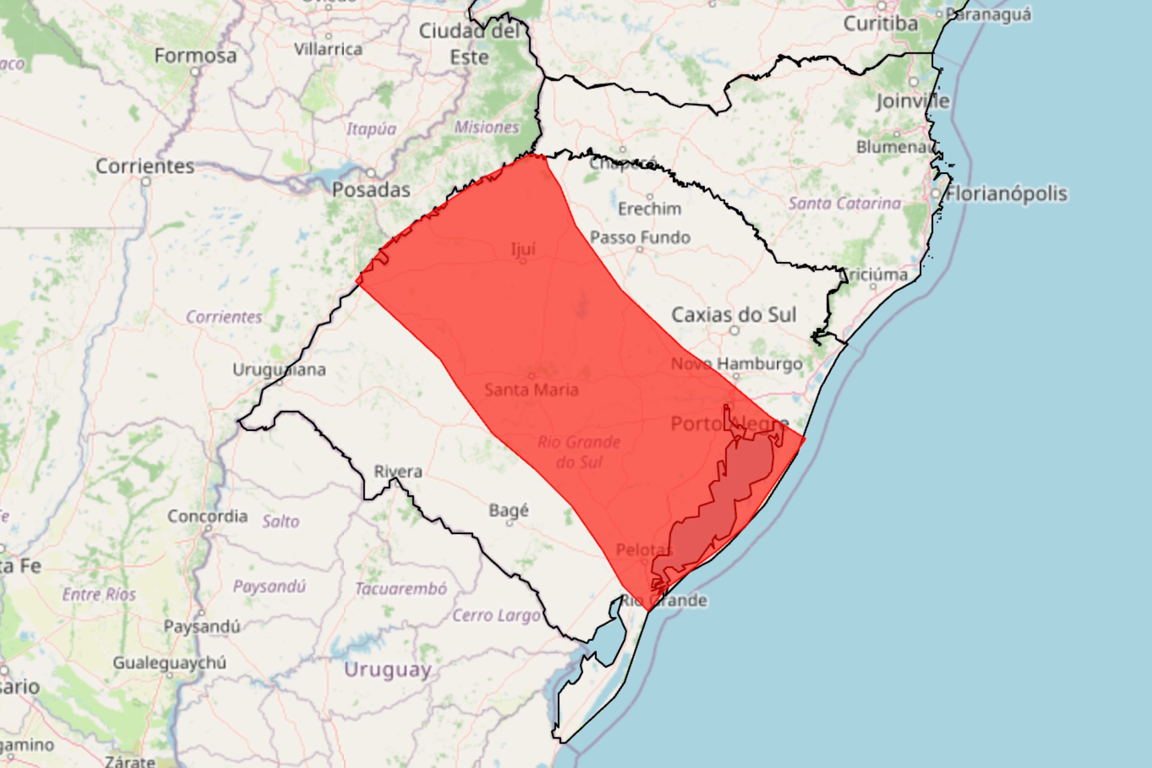 Mapa do Rio Grande do Sul com uma faixa vermelha diagonal indicando a área mais afetada pelas chuvas, abrangendo cidades como Santa Maria, Porto Alegre e Pelotas. Países vizinhos como Uruguai e Argentina são visíveis, assim como o oceano Atlântico