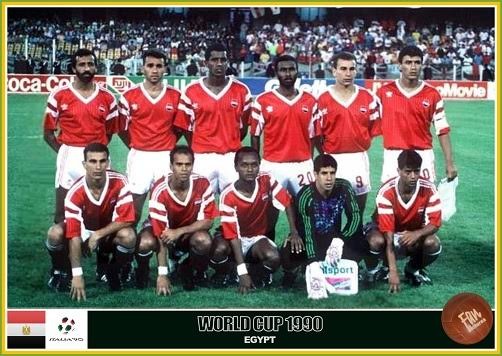 Time de futebol do Egito na Copa do Mundo de 1990, com sete jogadores em pé e quatro agachados, todos vestindo uniformes vermelhos e brancos, em um campo de grama verde com torcida ao fundo