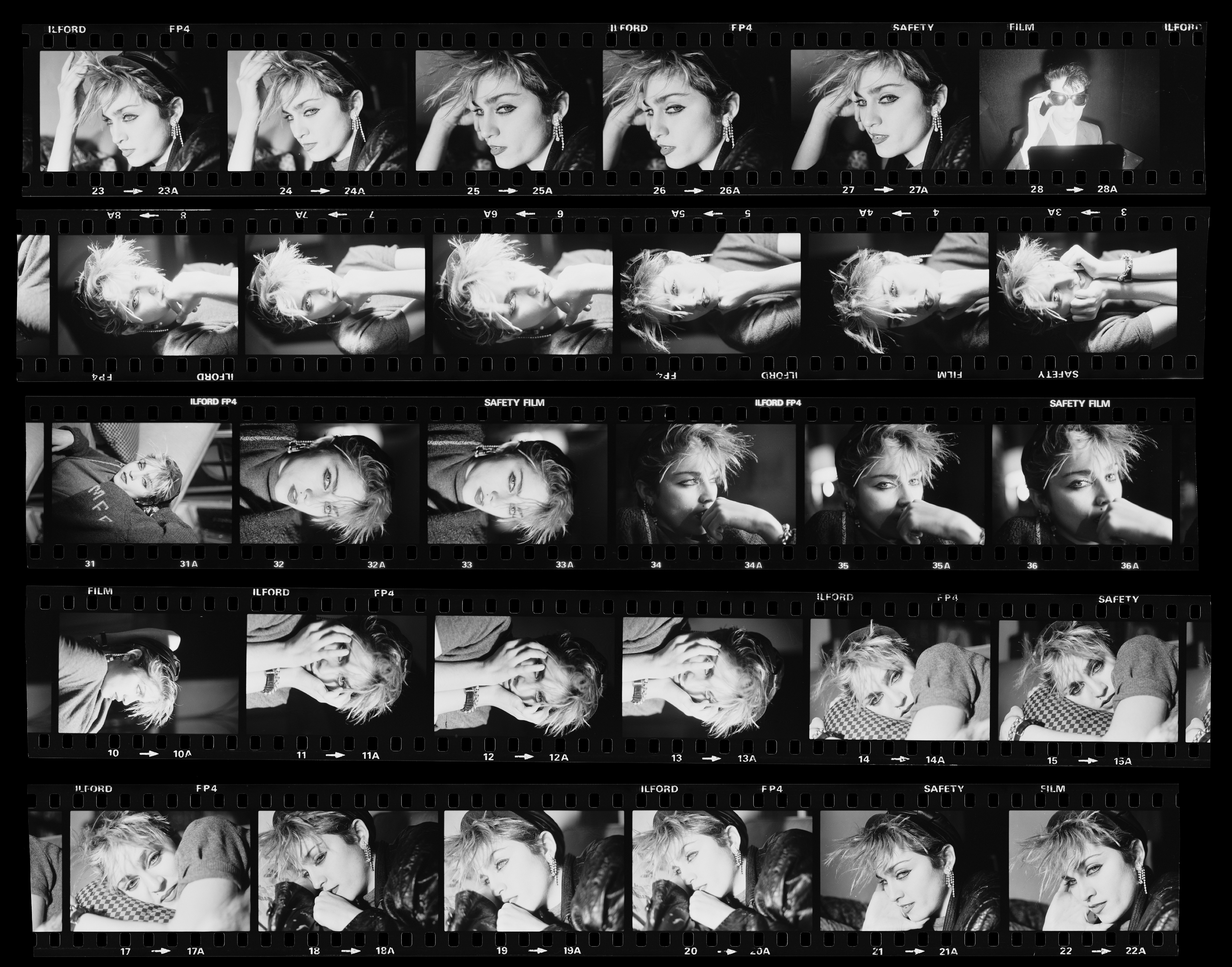 Folha de contato em preto e branco com v&aacute;rias fotos de Madonna jovem, com cabelo curto e maquiagem marcante, posando em diferentes &acirc;ngulos e express&otilde;es, algumas com as m&atilde;os no rosto ou cabelo, em um est&uacute;dio escuro