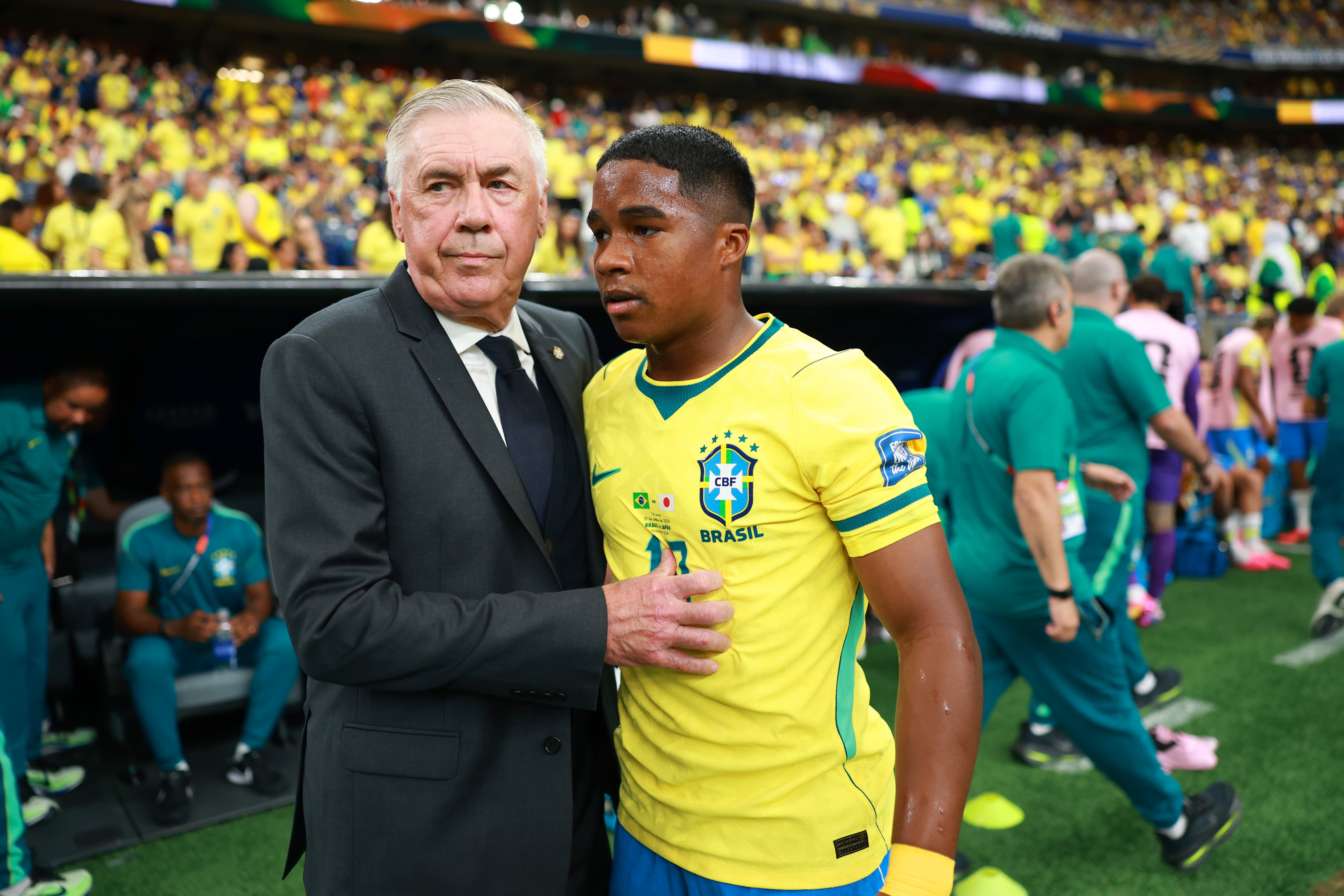 Homem de terno cinza e gravata preta abra&ccedil;a jogador jovem de camisa amarela da sele&ccedil;&atilde;o brasileira, em campo de futebol lotado de torcedores