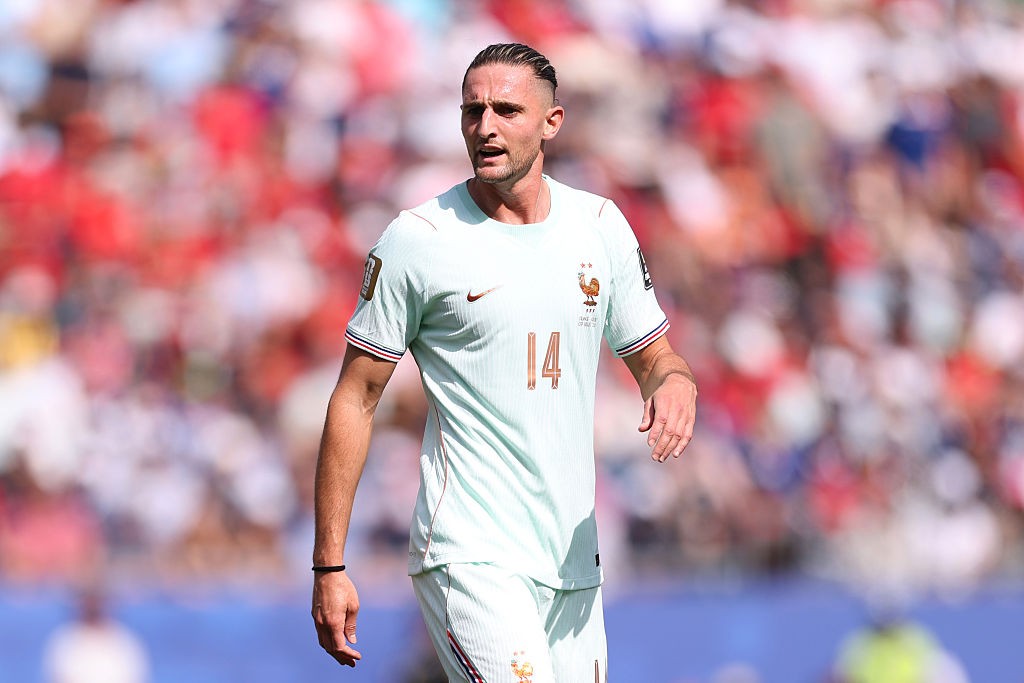 Jogador de futebol com camisa verde-água e número 14, cabelo penteado para trás, olhando para a direita, em campo com torcida desfocada ao fundo