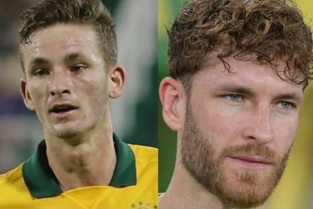 Dois homens brancos, um jovem com cabelo curto e suado em camisa amarela e gola verde, e outro com barba ruiva e cabelo cacheado, olhando para o lado