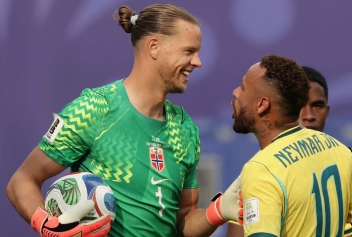 Dois jogadores de futebol sorriem e se cumprimentam em campo. Um goleiro loiro de coque, camisa verde e luvas laranja segura uma bola. O outro, Neymar Jr, veste camisa amarela com o número 10 e tem barba.