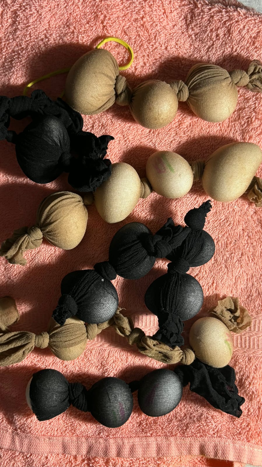 Ovos envoltos em meias-calças pretas e cor da pele, amarrados em fileiras, sobre uma toalha rosa felpuda