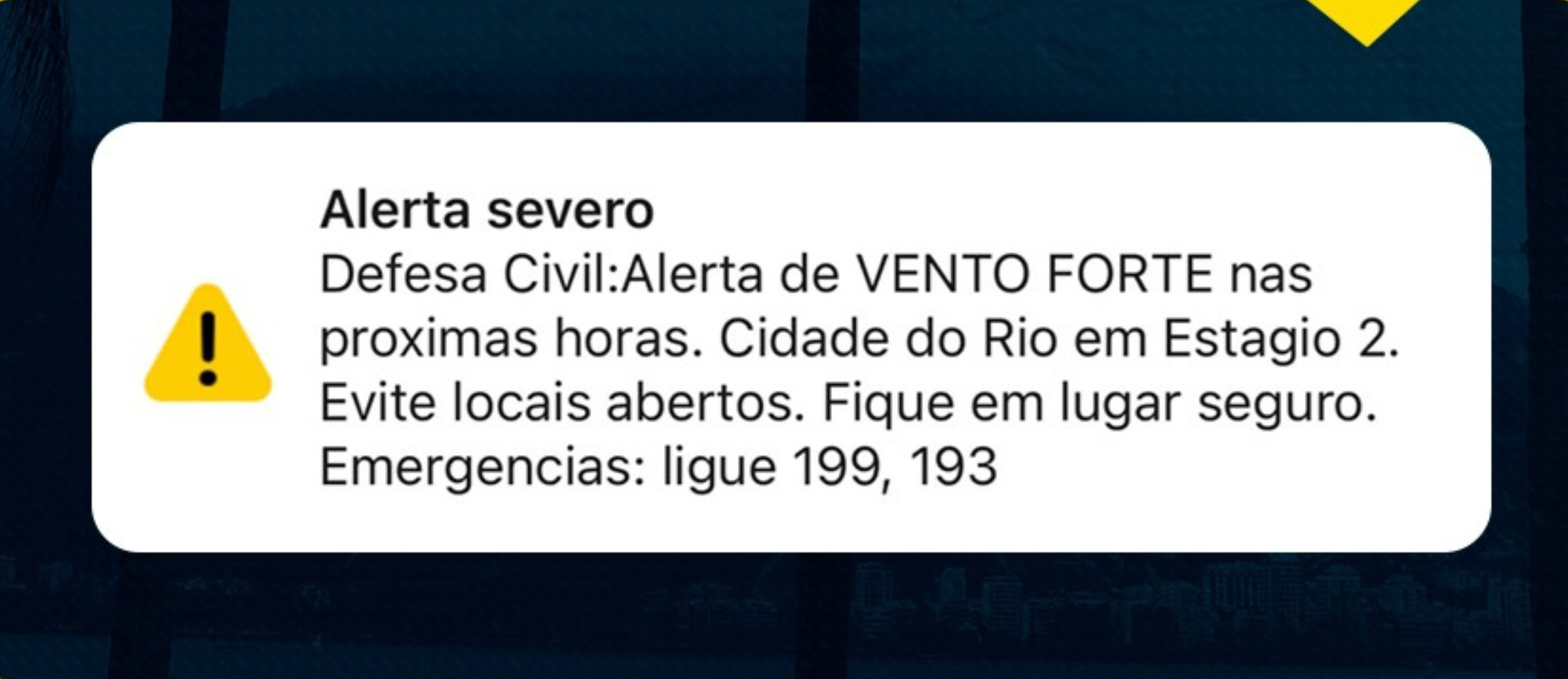 Alerta severo da Defesa Civil sobre vento forte no Rio de Janeiro, em Estágio 2. Recomenda-se evitar locais abertos e procurar abrigo seguro. Telefones de emergência: 199, 193. Um ícone de exclamação amarelo em triângulo preto acompanha a mensagem