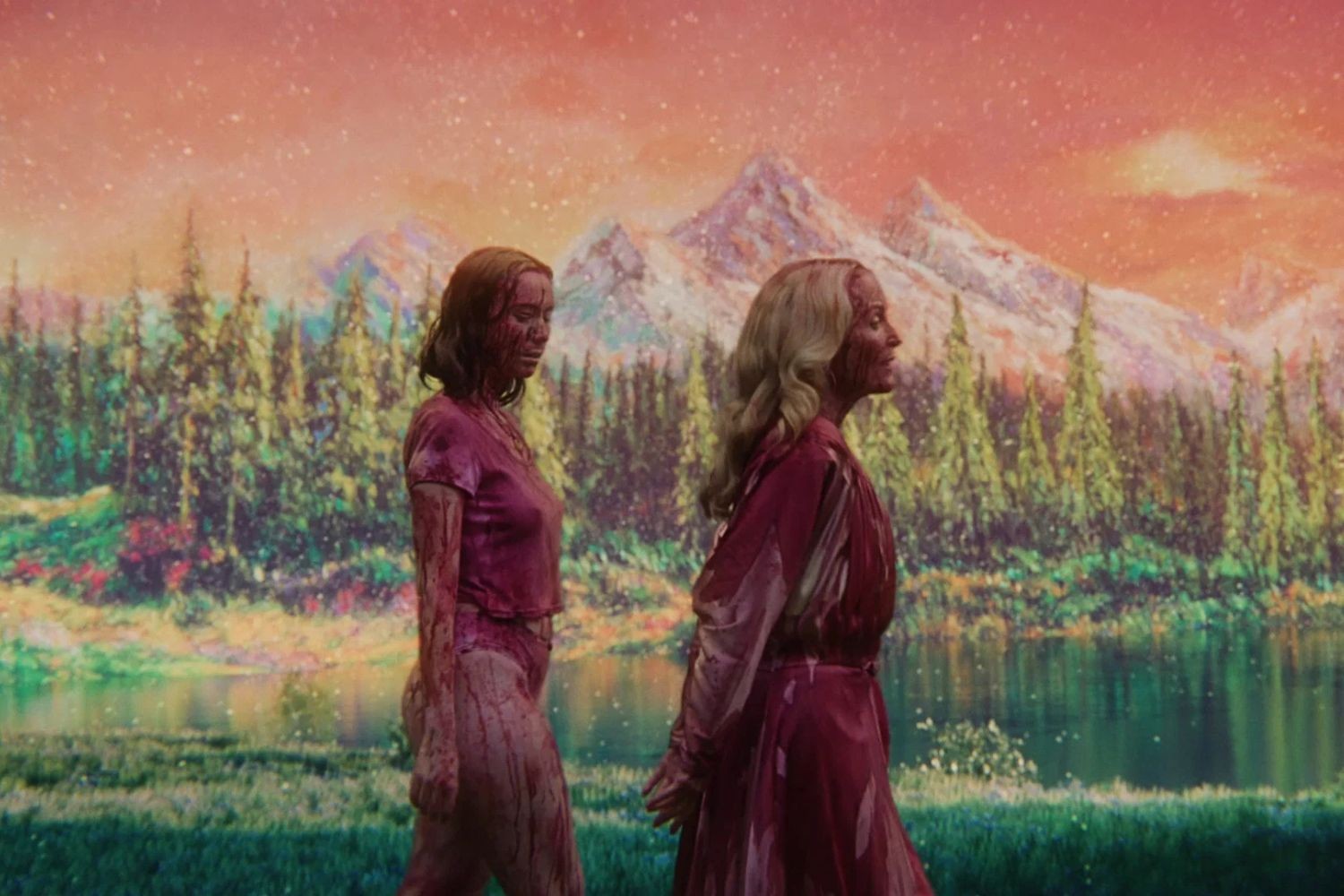 Duas mulheres, uma morena e uma loira, com roupas e corpos cobertos de sangue, caminham em um cenário de pintura com montanhas, floresta e lago, sob um céu alaranjado