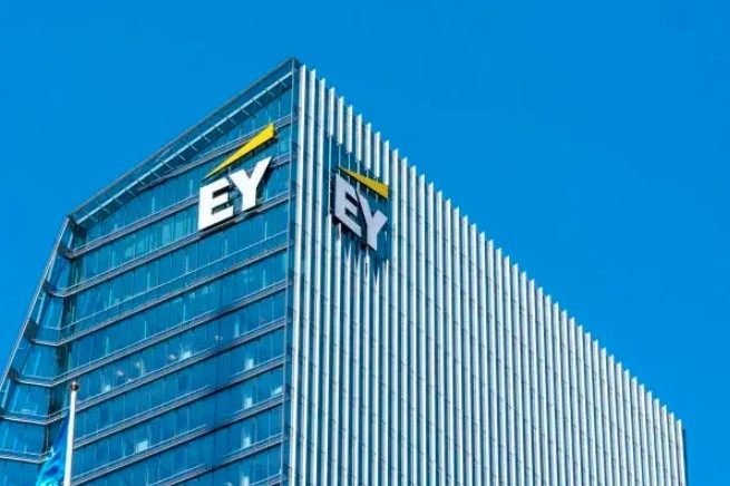 Edifício moderno de vidro azul com o logotipo branco e amarelo EY em duas faces, sob um céu azul claro