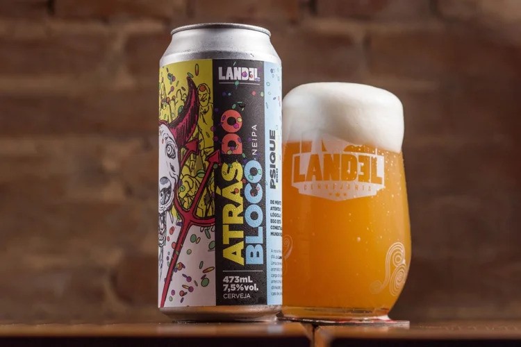 Lata de cerveja Landel Atrás do Bloco com ilustração de um diabo e um copo da mesma cerveja, com espuma, sobre uma mesa de madeira e fundo de tijolos