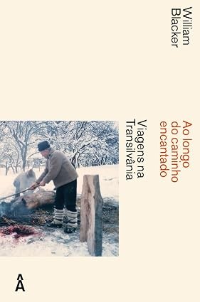 Capa do livro Ao longo do caminho encantado: Viagens na Transilvânia de William Blacker. Um homem de gorro e casaco, com meias grossas sobre as calças, usa um bastão para mexer em um fogo no chão nevado. Árvores cobertas de neve ao fundo.