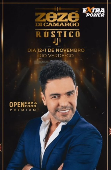 Cantor Zezé Di Camargo sorrindo, vestindo blazer azul e camisa branca aberta, braços cruzados. Ao fundo, texto dourado Zezé Di Camargo Rústico, Dia 12+1 de Novembro Rio Verde-GO e Open Bar & Food Premium