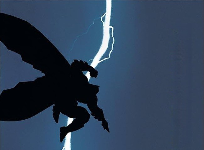 Silhueta escura do Batman com capa esvoaçante, punho cerrado, em pose de ataque, contra um céu noturno azul-escuro iluminado por um raio branco e sinuoso