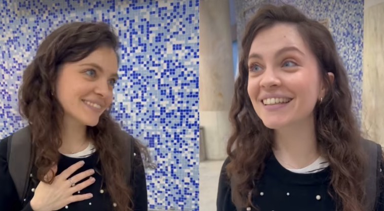 Mulher jovem de cabelos castanhos ondulados, sorrindo, com uma mochila nas costas e blusa preta com p&eacute;rolas. &Agrave; esquerda, ela olha para a direita com a m&atilde;o no peito, em frente a uma parede de azulejos azuis e brancos. &Agrave; direita, ela olha para cima e para a direita, com um pilar claro ao fundo