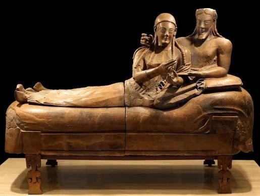 Sarc&oacute;fago etrusco de terracota, representando um casal reclinado em um leito. A mulher, &agrave; esquerda, usa touca e segura um objeto. O homem, &agrave; direita, tem cabelos longos e barba, com o bra&ccedil;o esquerdo sobre o ombro da mulher. Ambos sorriem, em pose relaxada, sobre um sarc&oacute;fago decorado com pernas esculpidas