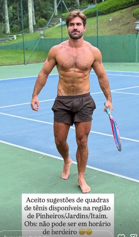 Homem musculoso, sem camisa, de shorts escuros e descalço, caminha em quadra de tênis azul e verde, segurando uma raquete colorida. Ele tem barba e cabelo castanho claro, com expressão séria. Ao fundo, árvores e uma cerca verde. Um texto sobre sugestões de quadras de tênis cobre a parte inferior da imagem