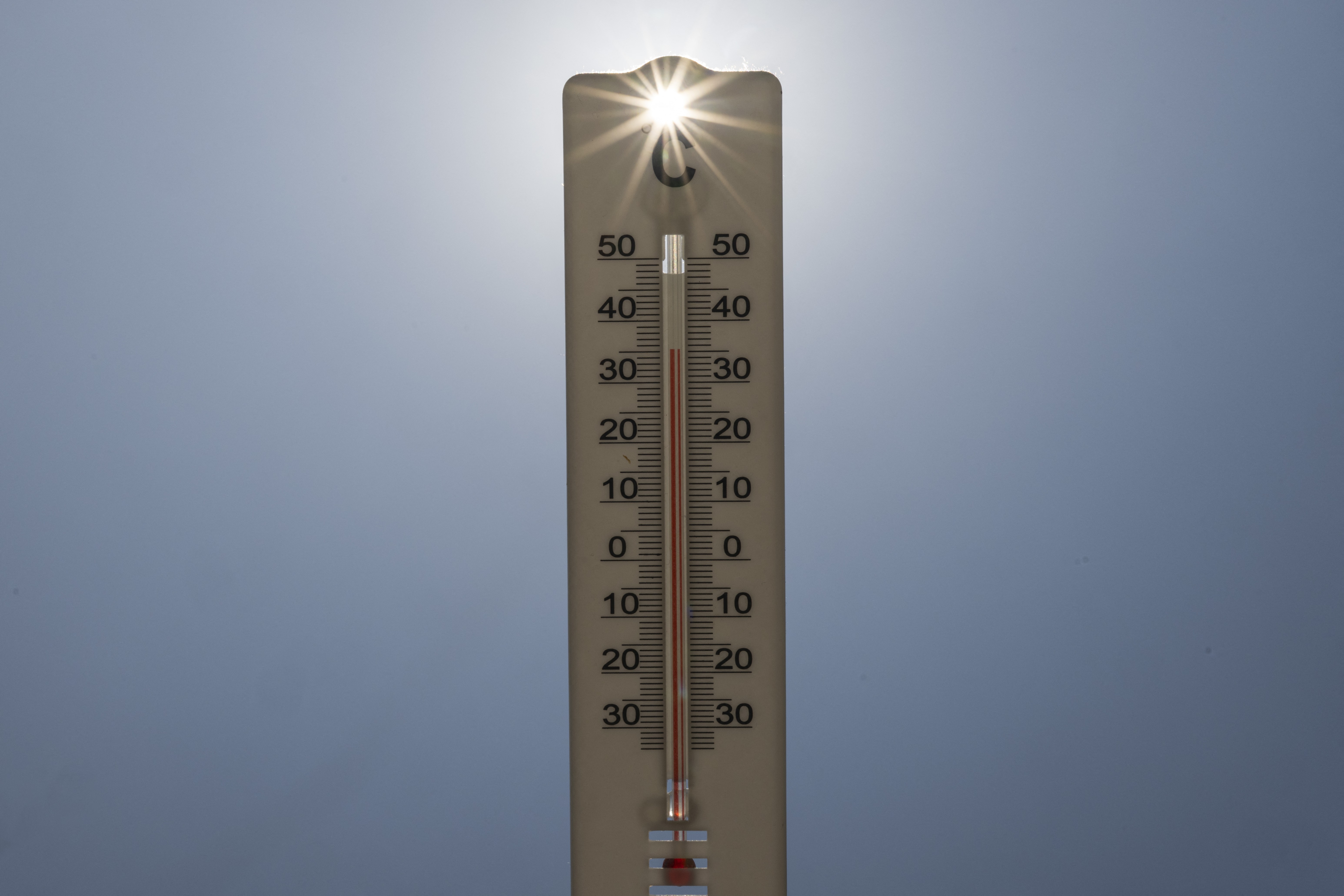 Termômetro de mercúrio marcando aproximadamente 40 graus Celsius, com o sol brilhando intensamente no topo e um céu azul claro ao fundo