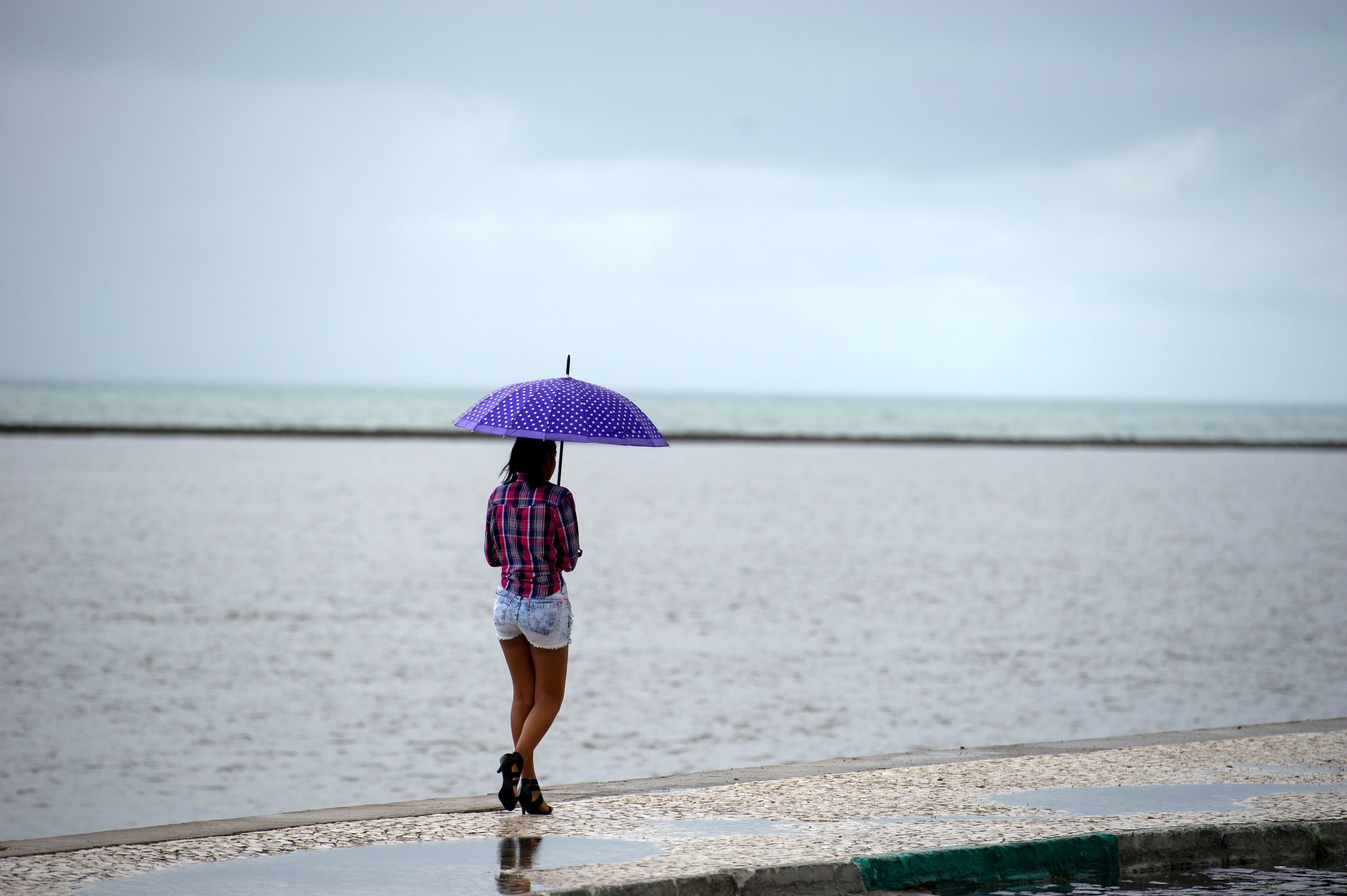 A girl walks by the shore with an umbrella while it rains in Porto Seguro, Brazil, 20 June 2014. The FIFA World Cup 2014 will take place in Brazil from 12 June to 13 July 2014. Photo: Thomas Eisenhuth/dpa | usage worldwide (Photo by Thomas Eisenhuth/picture alliance via Getty Images)