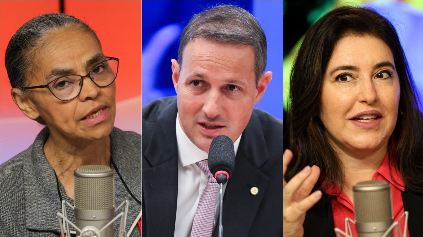 Três políticos em close-up, da esquerda para a direita: mulher negra de óculos e cabelos presos, em casaco cinza, falando ao microfone, homem branco de terno escuro e gravata clara, com broche dourado na lapela, falando ao microfone; e mulher branca de cabelos escuros soltos, blusa vermelha e blazer preto, gesticulando enquanto fala ao microfone