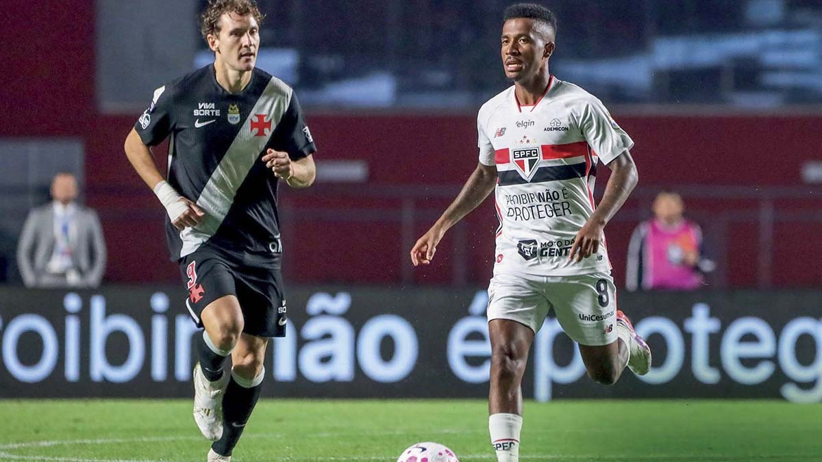 Dois jogadores de futebol correndo em campo verde. Um veste camisa preta e branca do Vasco, o outro camisa branca e vermelha do São Paulo, com uma bola rosa aos pés.