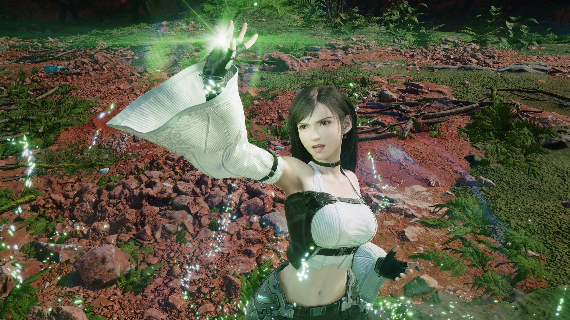 Personagem feminina de cabelos escuros e top branco, com luva branca no braço esquerdo estendido para cima, emitindo luz verde. Ela está em um cenário de terra avermelhada e vegetação, com pontos de luz verde flutuando ao redor